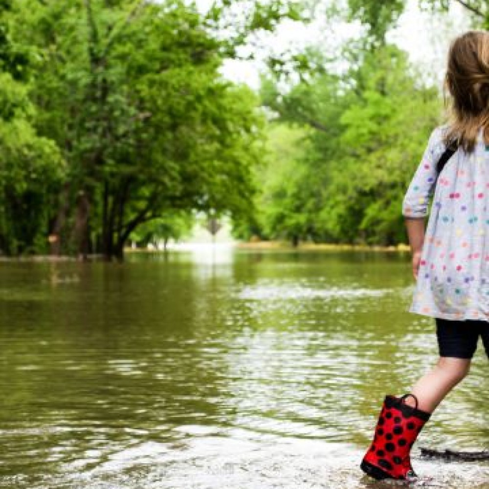 Meisje in regenlaarzen in een bosrijke omgeving die is ondergelopen met water