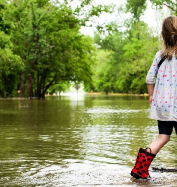 Meisje in regenlaarzen in een bosrijke omgeving die is ondergelopen met water