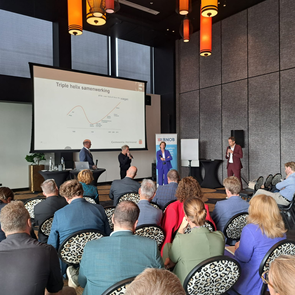 Deelnemers bestuurlijke Regioheidag luisteren naar drie sprekers die voor de deelnemers staan