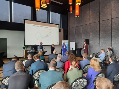 Deelnemers bestuurlijke Regioheidag luisteren naar drie sprekers die voor de deelnemers staan