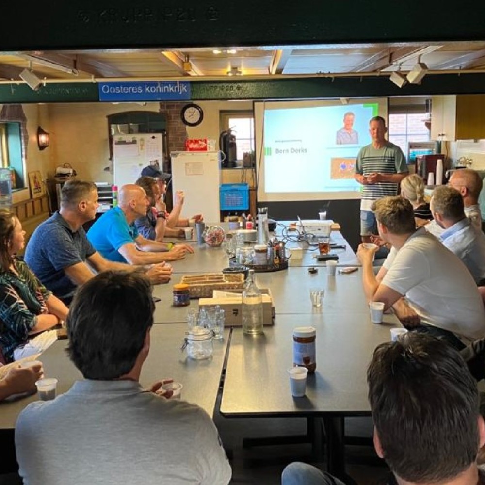 Raadsleden uit Noordoost-Brabant luisteren naar een presentatie van een boer in een zaal op zijn boerderij 
