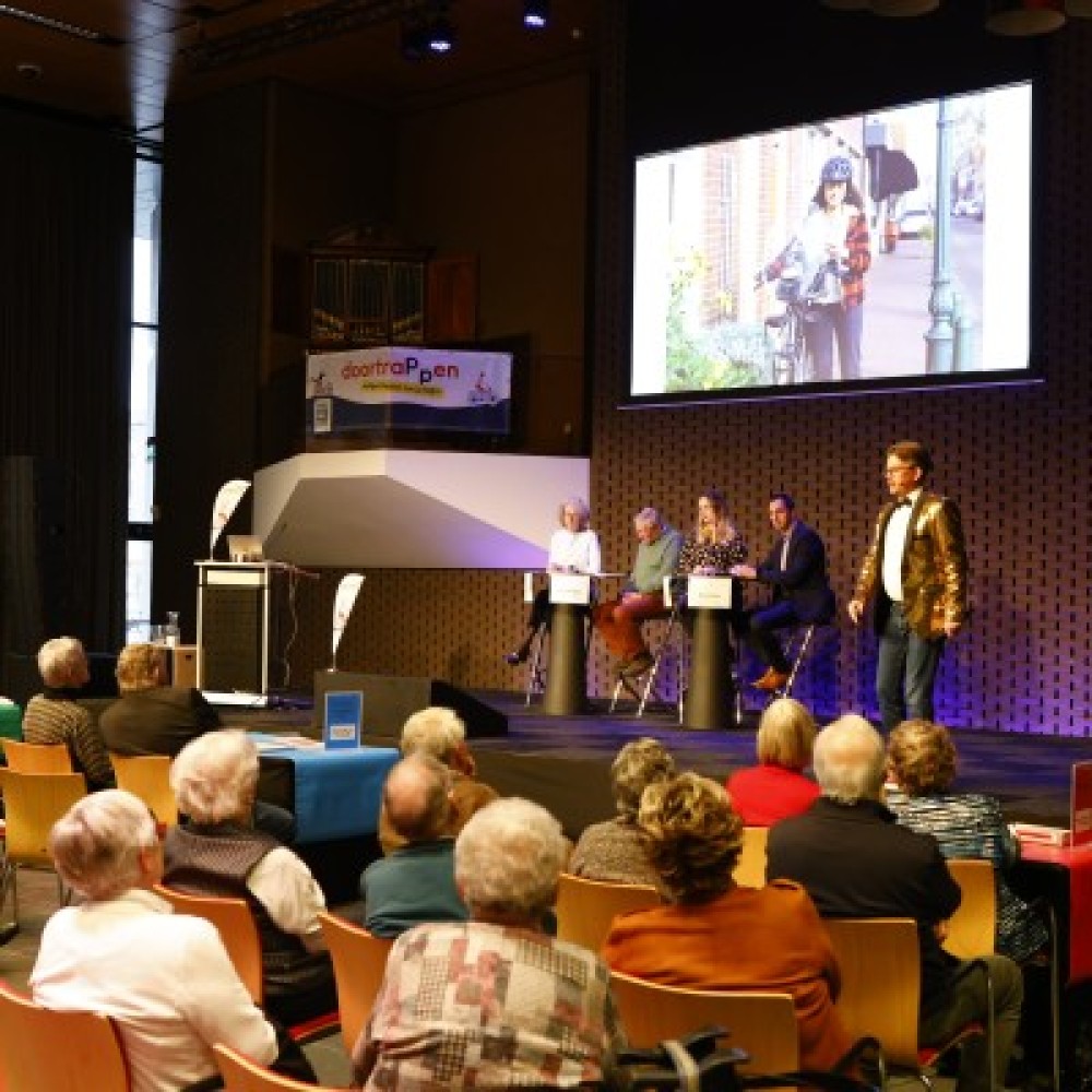 Paneldiscussie met verkeerspartijen op een podium in een zaal met deelnemers aan de quiz 