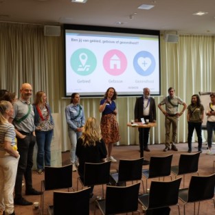 Sprekers en deelnemers Hittedialoog vooraan in een zaal met elkaar in gesprek