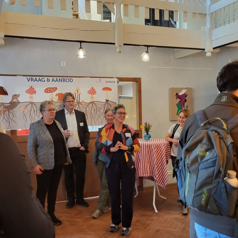 Deelnemers van de netwerkbijeenkomst staan bij een tafel met daarachter een informatiebord
