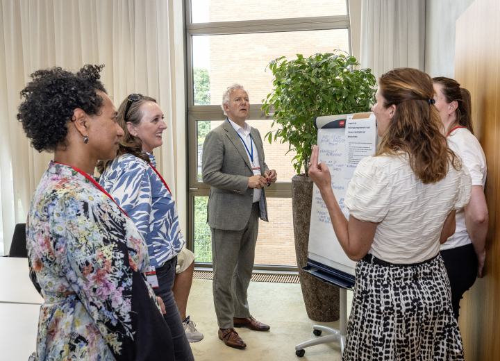 Deelnemers aan de ambtelijke bijeenkomst werken in een klein groepje aan een opdracht bij een flipover   