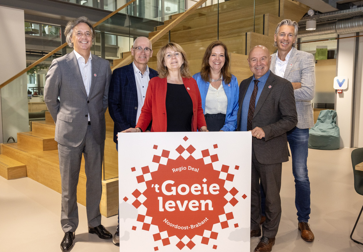 De leden van de stuurgroep Regio Deal 't Goeie leven op een rij voor een trap, een bord vasthoudend met het Regio Deal logo