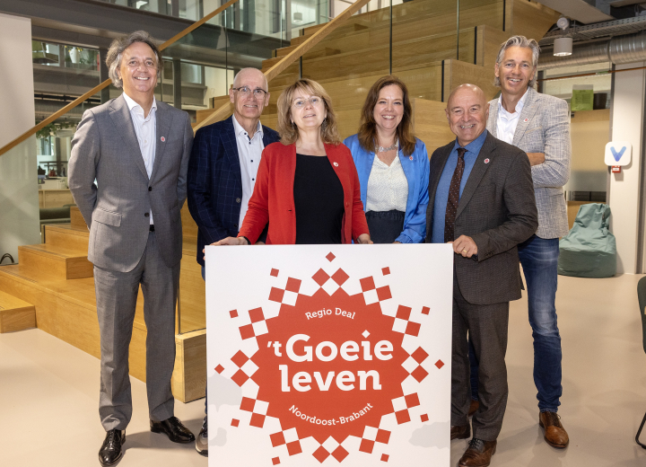 Foto van de Stuurgroep (bestuur) van Regio Deal ’t Goeie Leven in Noordoost-Brabant. Zij staan bij een trap in een binnenruimte, met een bord met het logo van ’t Goeie Leven op de voorgrond.