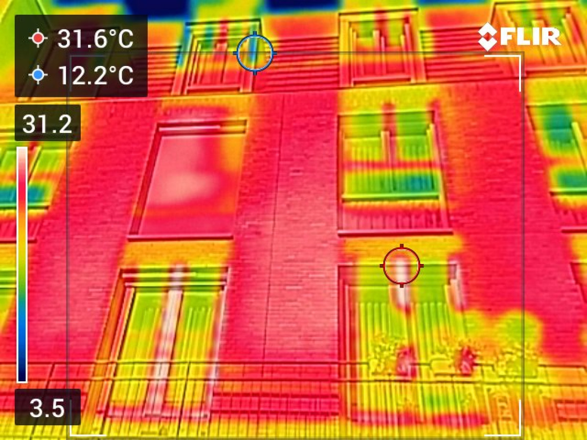 Thermografische opname van een gevel, waarbij verschillende kleuren (rood, geel groen, blauw) temperatuurverschillen rond ramen en muren zichtbaar maken
