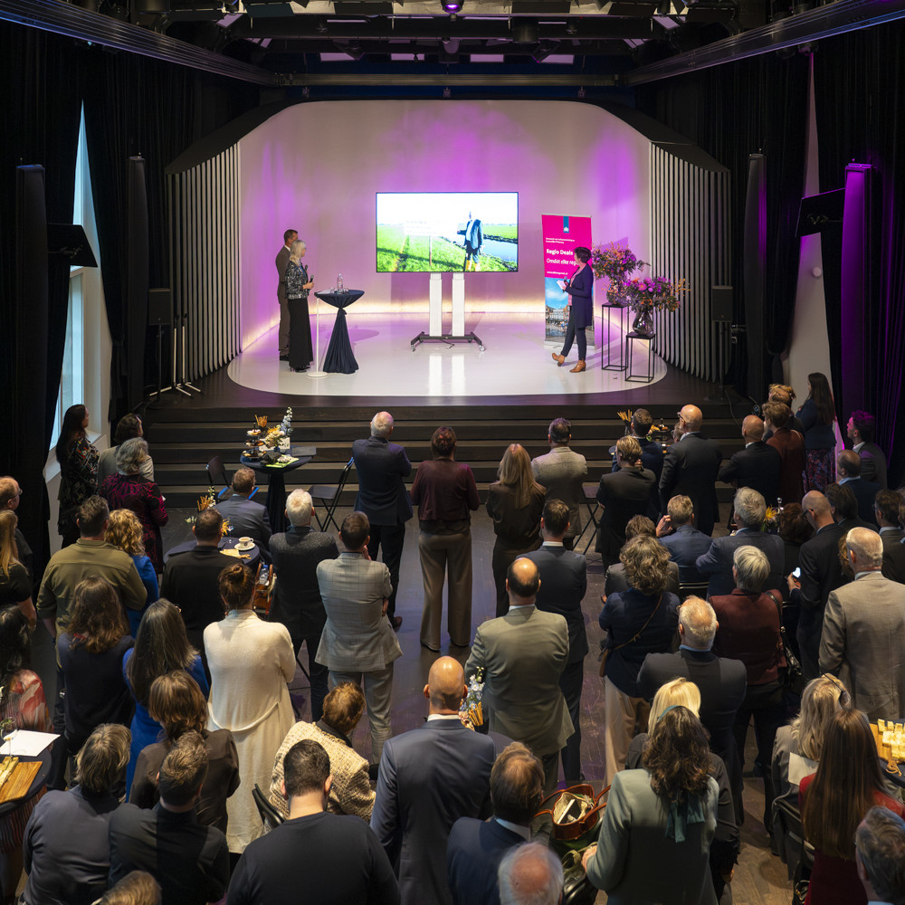 Grote groep aanwezigen die naar een presentatie kijkt op een podium tijdens de officiële Regio Deal bijeenkomst