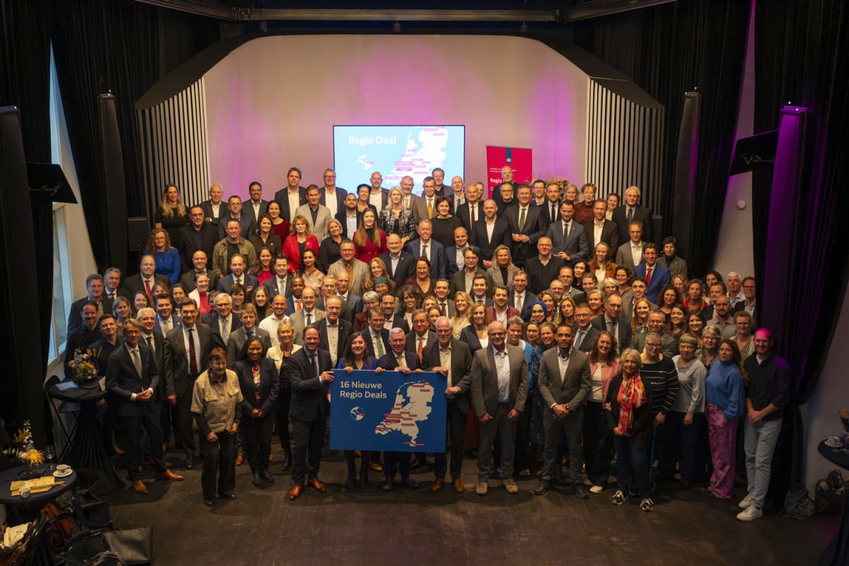 Groepsfoto met alle deelnemers aan de officieél startbijeenkomst van de Regio Deals met ene persoon vooraan die een bord van de Regio Deals vasthoudt