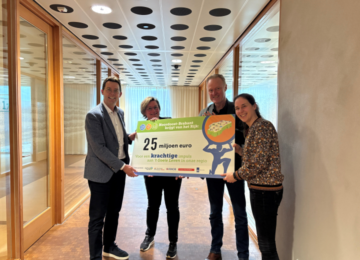 Vier mensen in een kantooromgeving die een grote cheque vasthouden van 25 miljoen euro 