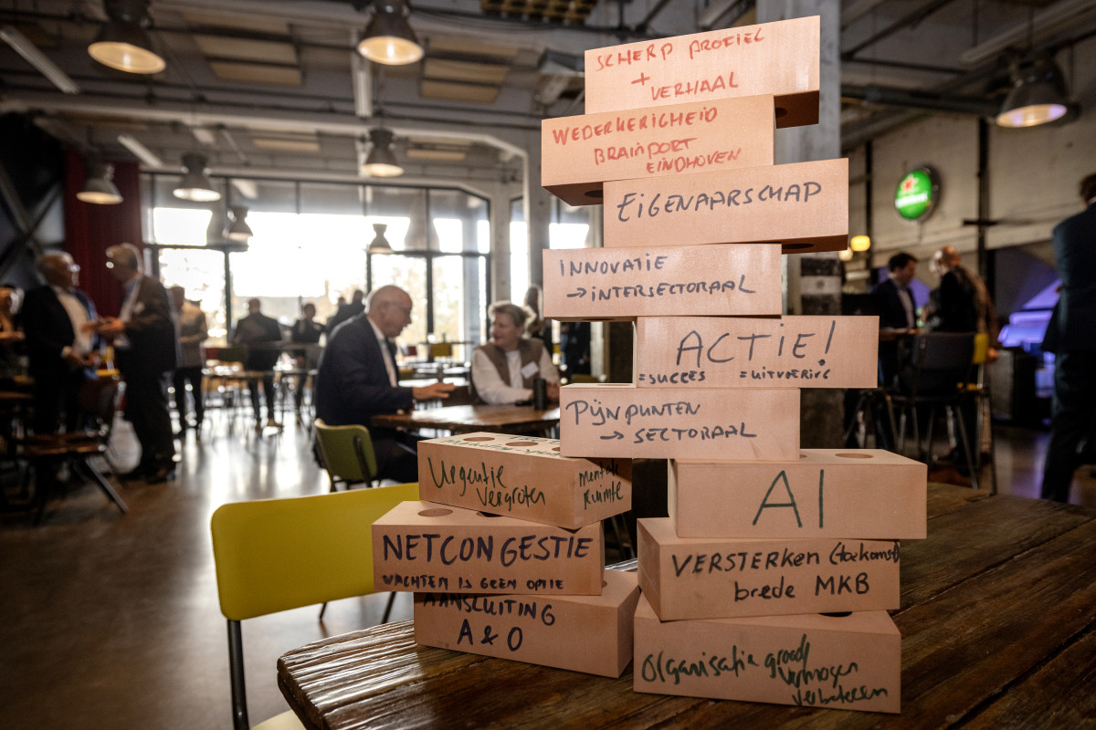 Houten blokken met strategische kernwoorden zoals innovatie, AI en netcongestie opgestapeld op een tafel op de voorgrond en deelnemers aan de consultatiebijeenkomst op de achtergrond