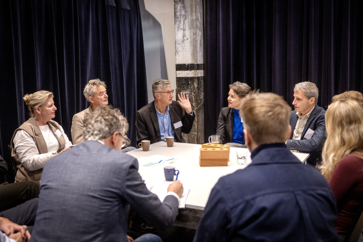 Groep deelnemers, mannen en vrouwen, aan tafel met koffie en bakstenen op de tafel met elkaar in gesprek