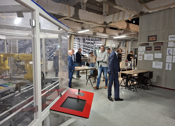 De leden van de Stuurgroep Regio Deal krijgen een rondleiding in The Chocolate factory. Ze staan in een high tech productieruimte bij een robotica-installatie.