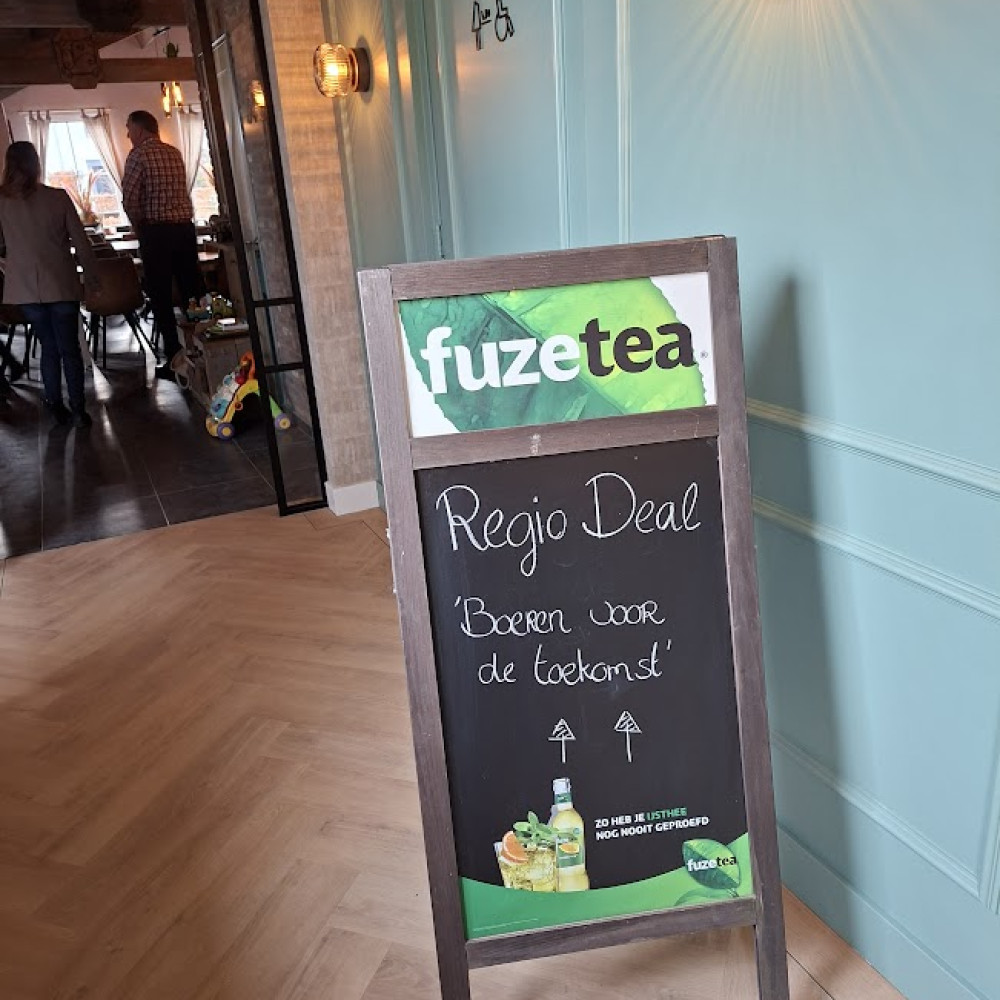 Een groot krijtbord op de grond met een welkomsttekst en pijlen als wegwijzers voor de deelnemers aan de bijeenkomst. Op de bovenkant reclame voor het drankje Fuzetea.