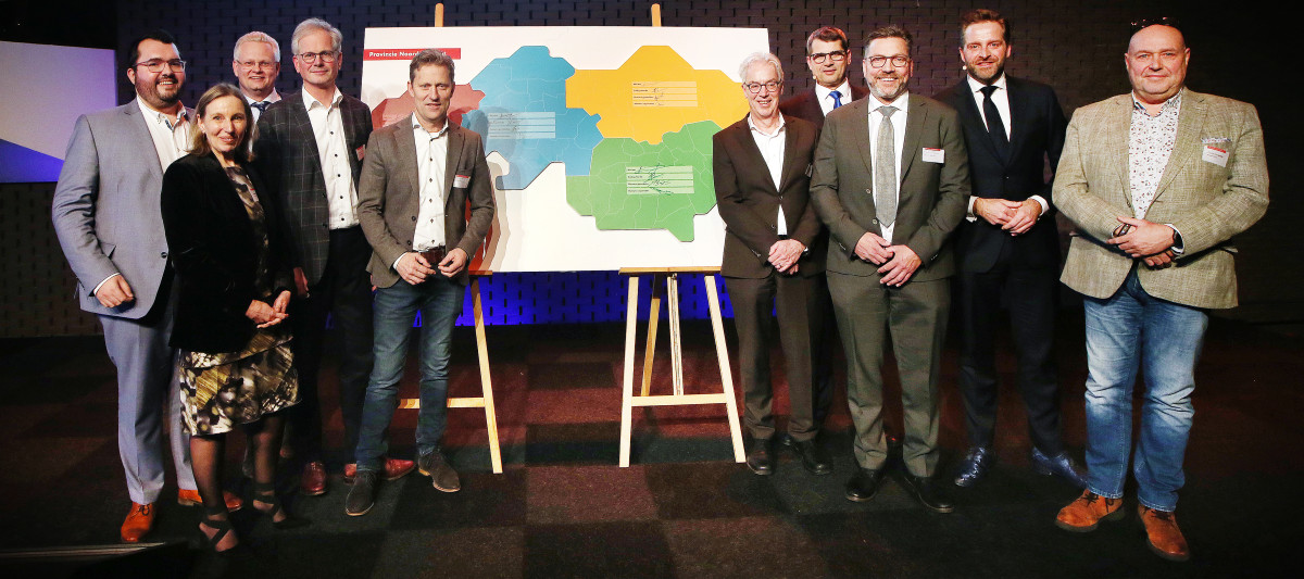 De ondertekenaars van de vier Brabantse Woondeals op een rij op een podium met in het midden een kaart van Brabant optwee houden schilderezels 