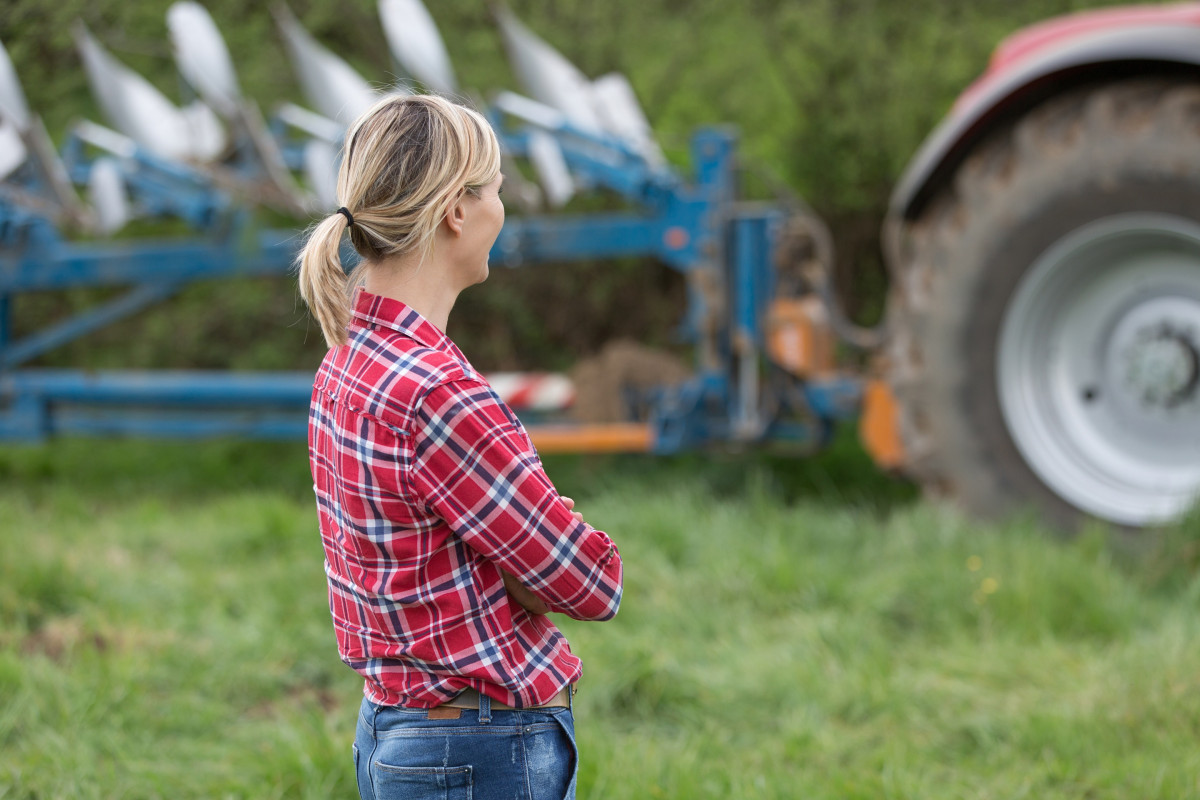 Vrouw op landbouwbedrijf kijkt uit over tractor en landbouwmachine op grasveld.