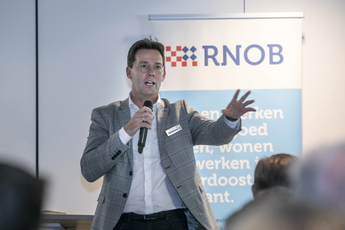 René Peerenboom voor een groep met mensen met een rollup banner van RNOB op de achtergrond