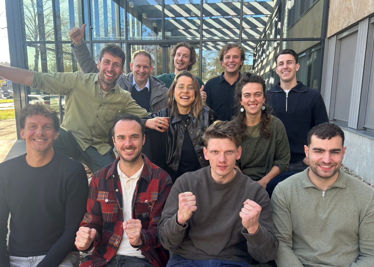 De 11 jonge ondernemers van Jump poseren buiten tijdens een energieke teambijeenkomst bij een moderne glazen gevel van Jamfabriek in Den Bosch.