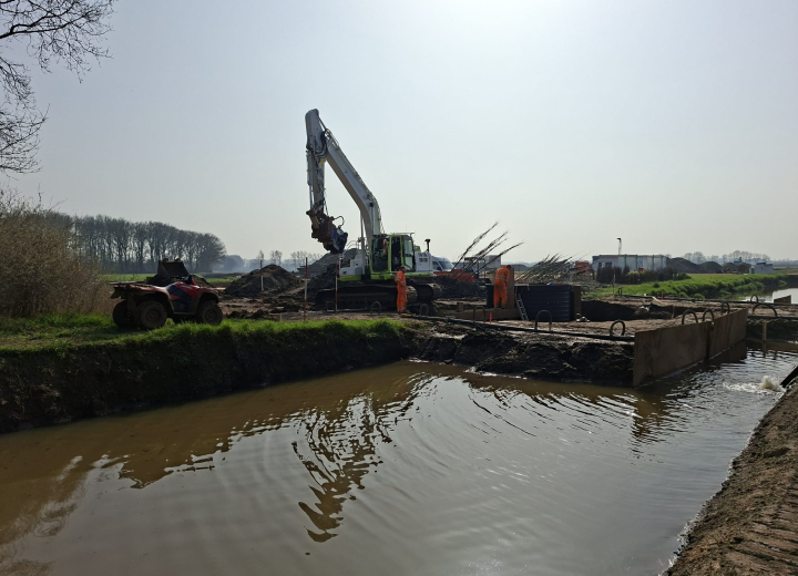 Graafmachine en medewerkers aan het werk bij water- en natuurherstel langs de Aa in een landelijk gebied