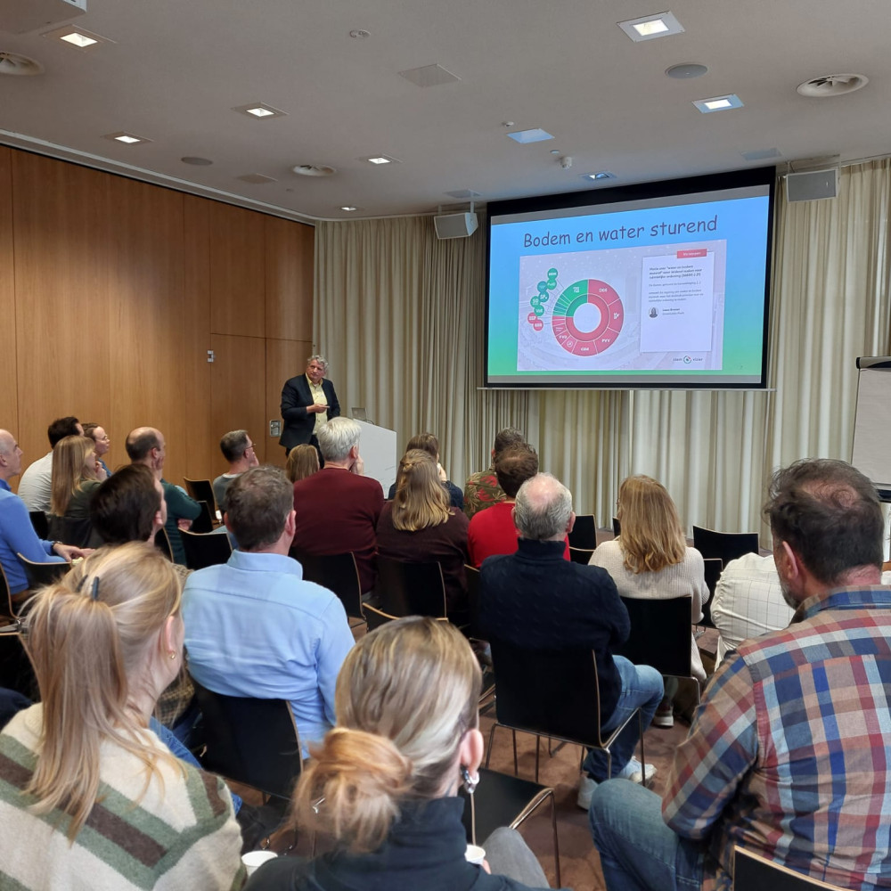 Presentatie over bodem- en watersturing voor een groep aanwezigen in een conferentieruimte.