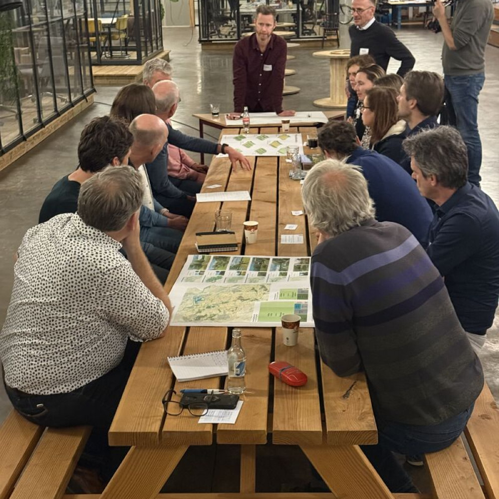 Deelnemers van de Peelwerkplaats bespreken gebiedskaarten tijdens een interactieve werksessie aan een lange tafel.
