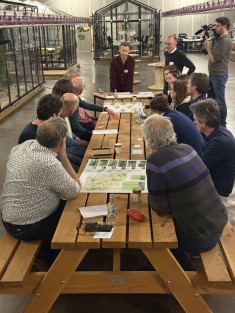 Deelnemers van de Peelwerkplaats bespreken gebiedskaarten tijdens een interactieve werksessie aan een lange tafel.