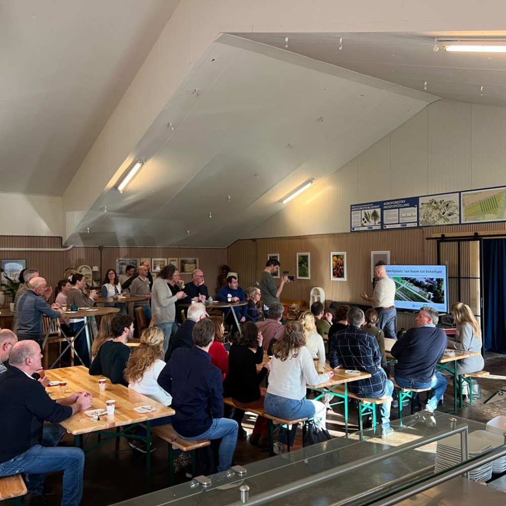 Groep deelnemers van de Peelwerkplaats luistert naar presentatie in een grote zaal.