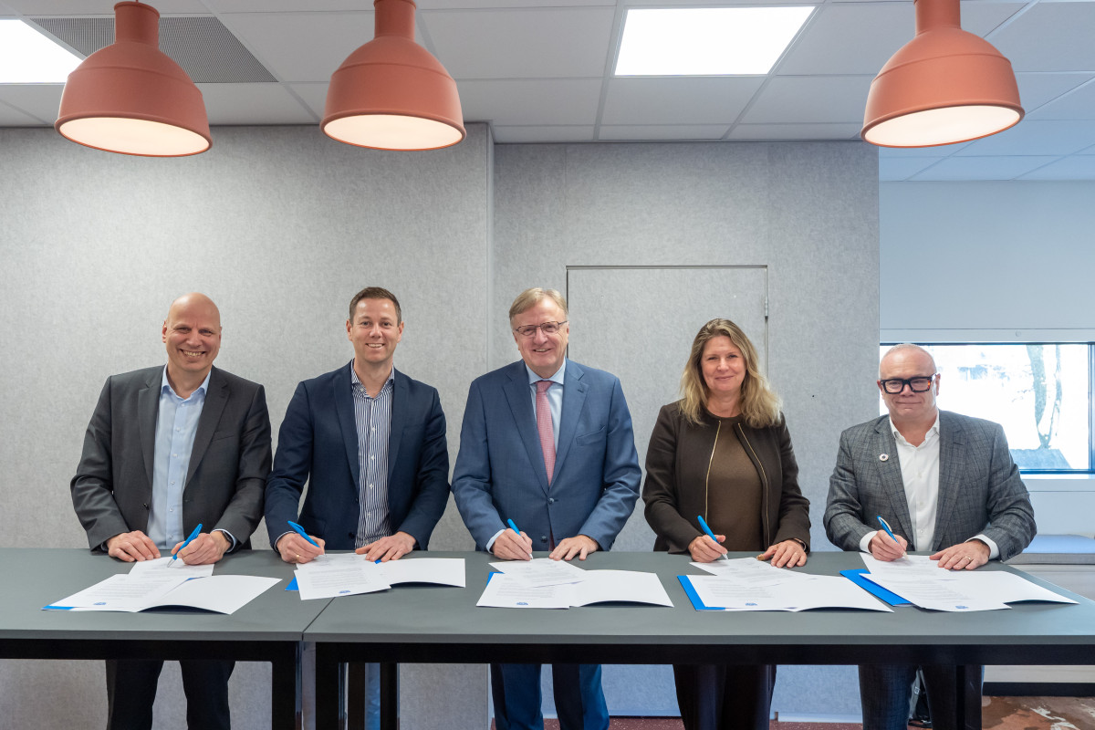 Vijf bestuurders ondertekenen een convenant, staande aan een hoge tafel met elk een eigen versie van het document.