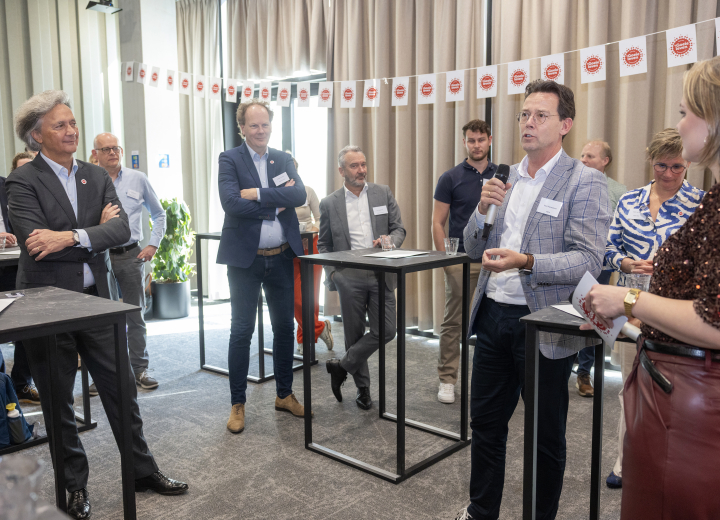 Deelnemers aan het startevent in een interactieve sessie met presentatie aan statafels. Op de achtergrond een lijn met vlaggetjes.