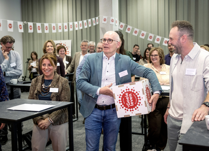 Deelnemers bijeenkomst met elkaar in gesprek, waarvan één een kartonnen witte doos vasthoudt met het Regio Deal logo