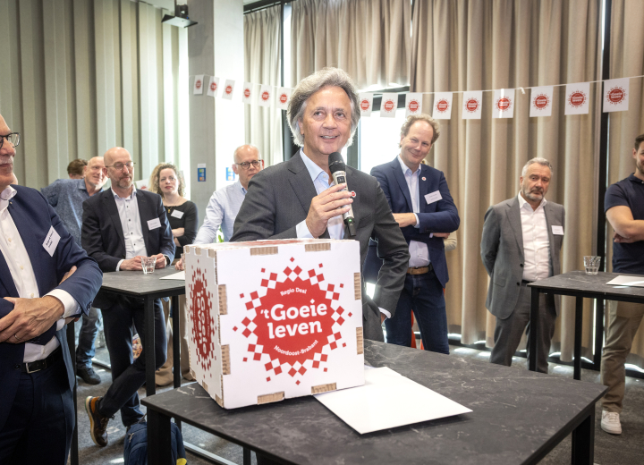 Deelnemers bijeenkomst met elkaar in gesprek, waarvan één een microfoon en kartonnen witte doos vasthoudt met het Regio Deal logo