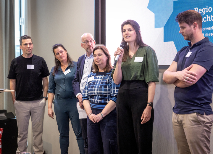 Vijf programmamanagers lichten op het podium de inhoud van hun programma's toe. Op de achtergrond een illustratie van de Regio Deal.