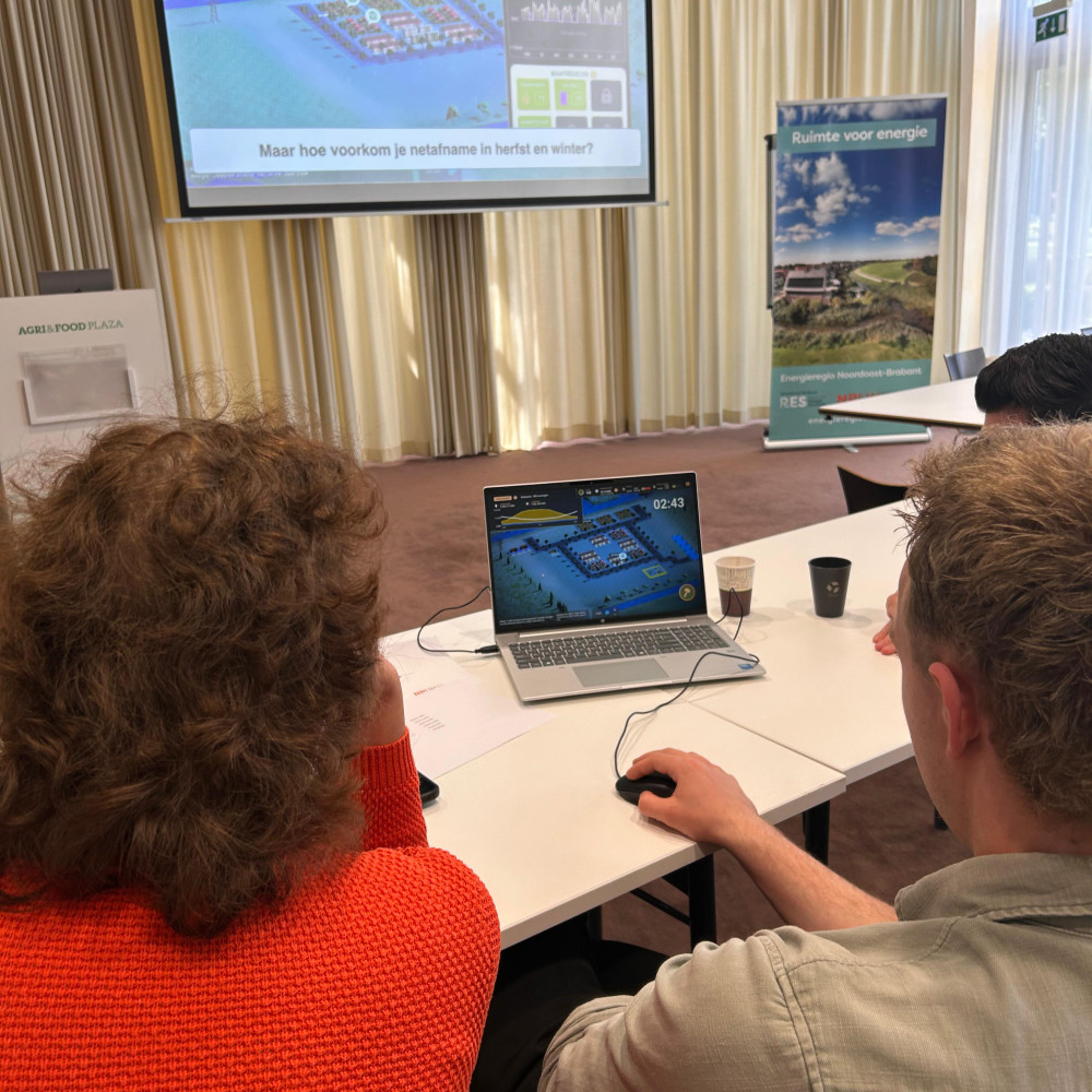 Deelnemers spelen een serious game op een laptop tijdens de workshop met op de achtergrond een presentatie.