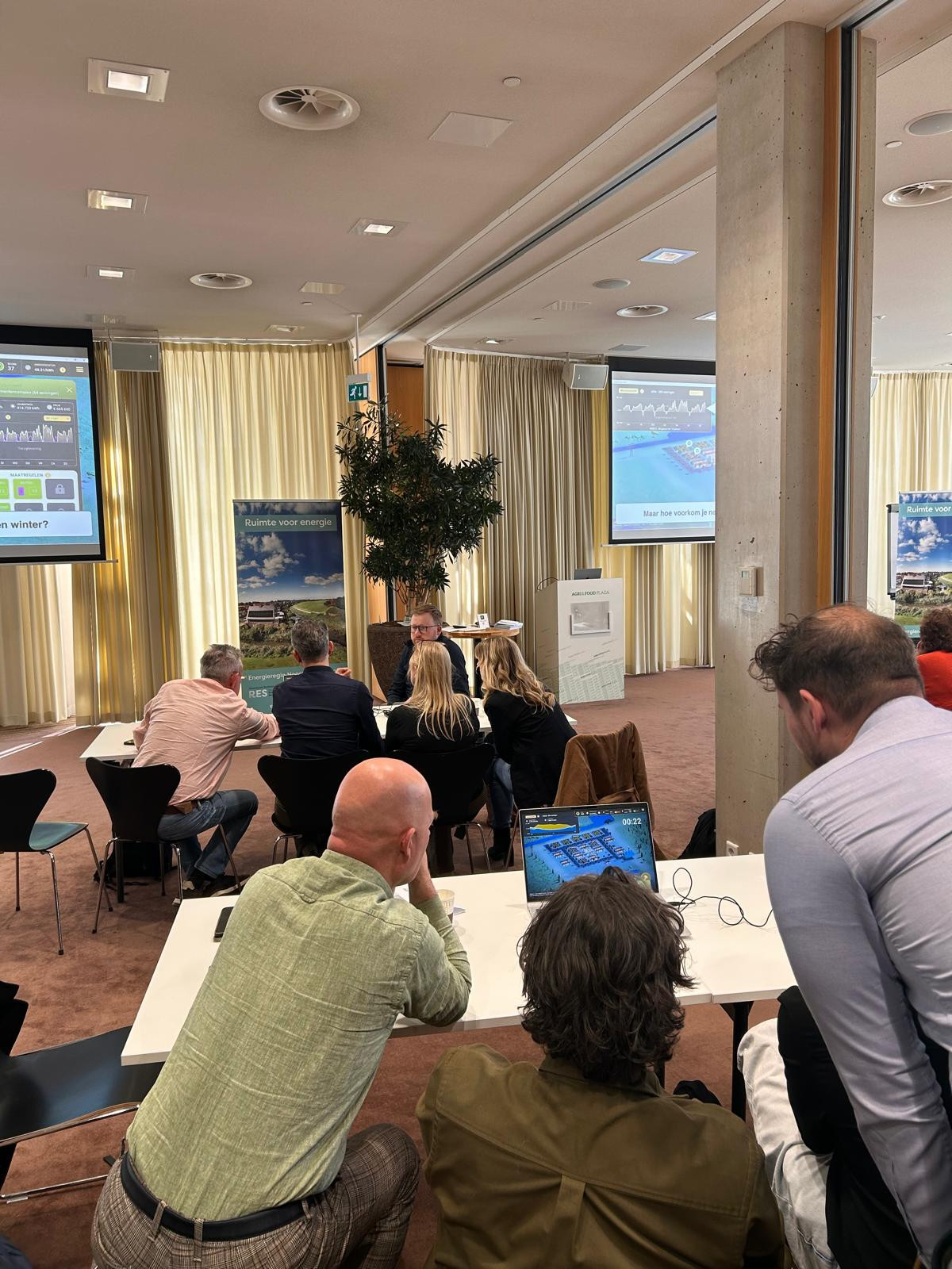 Deelnemers spelen een serious game op een laptop tijdens de workshop met op de achtergrond diverse presentaties.