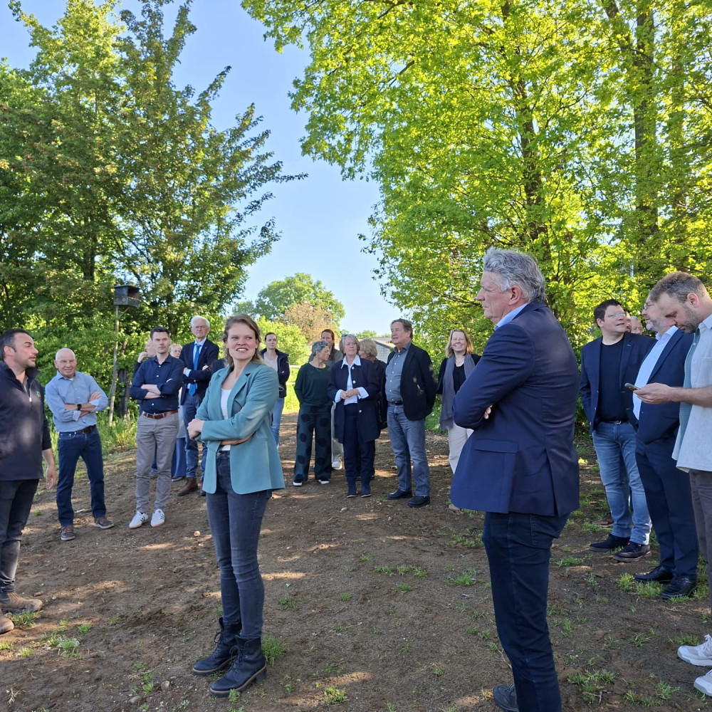Groep wethouders en boeren met elkaar in gesprek op een stuk landbouwgrond met daaromheen bomen