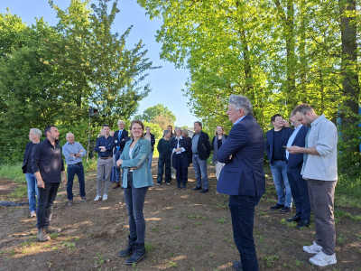 Groep wethouders en boeren met elkaar in gesprek op een stuk landbouwgrond met daaromheen bomen