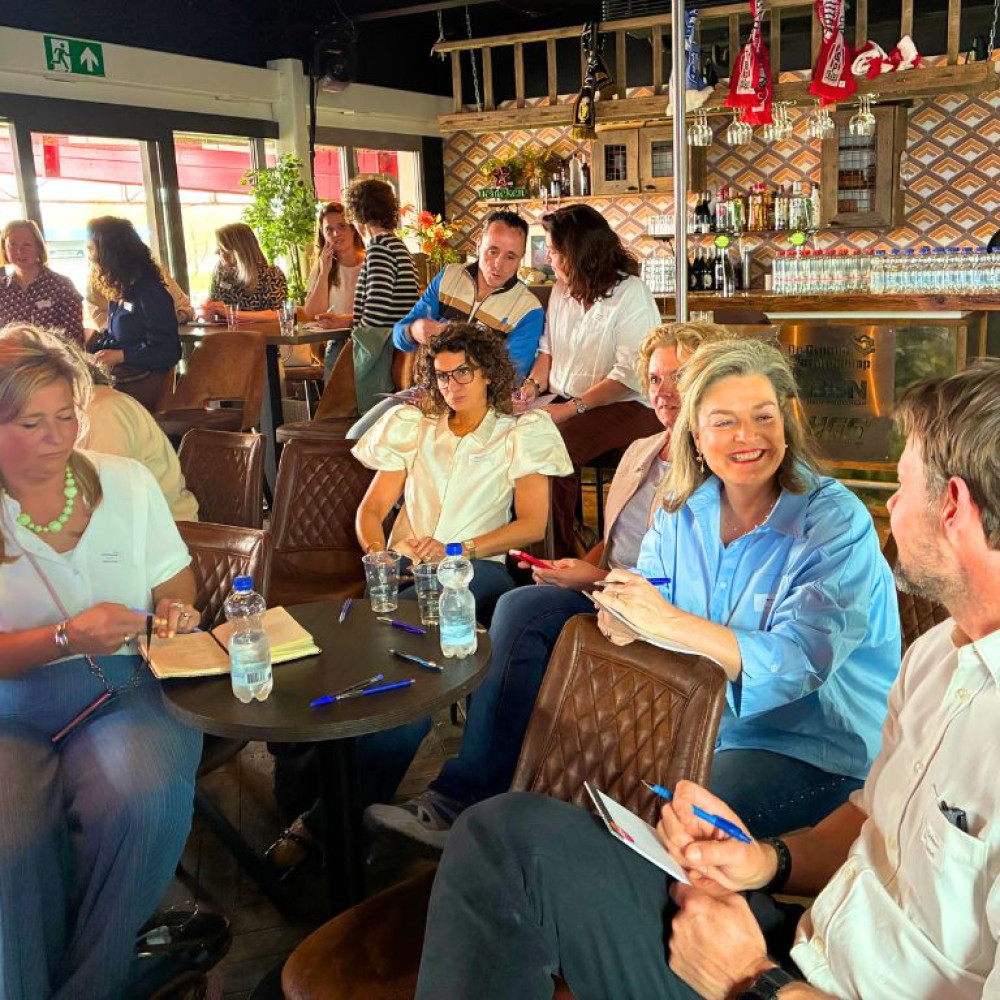 Deelnemers aan de regionale loopbaandag van Noordoost Brabant Werkt met elkaar in gesprek aan tafel met andere deelnemers op de achtergrond.