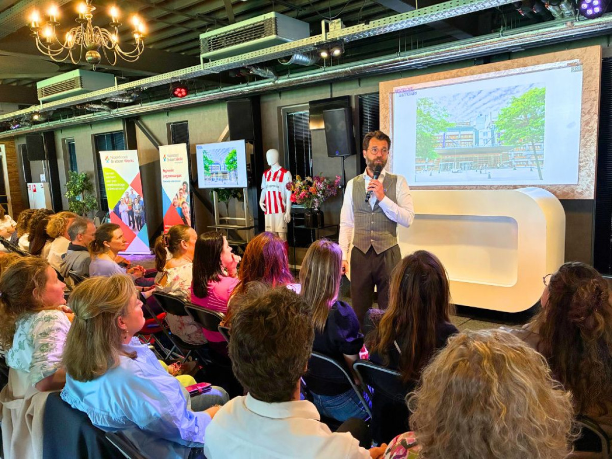 Key note spreker van de regionale loopbaandag van Noordoost Brabant Werkt geeft een presentatie aan de deelnemers vóór een projectiescherm.