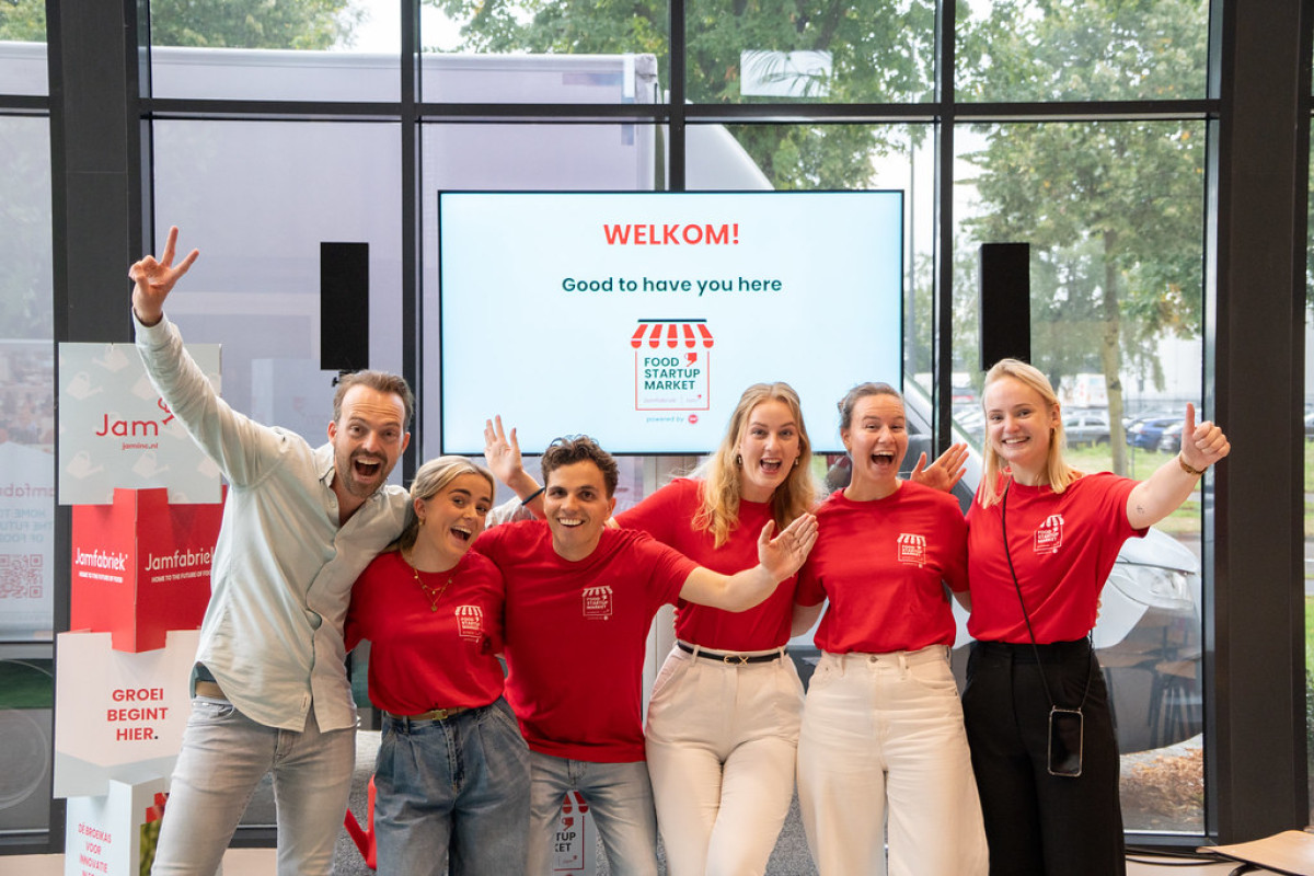 Groepsfoto van het organiserend team van de Food Startup Market bij Jamfabriek, juichend voor een presentatiescherm.