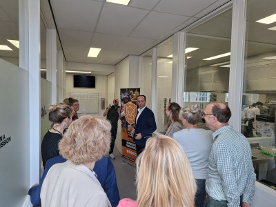 Groep mensen staat binnen rond een spreker die een rondleiding geeft door een gebouw van het Koning Willem I College.