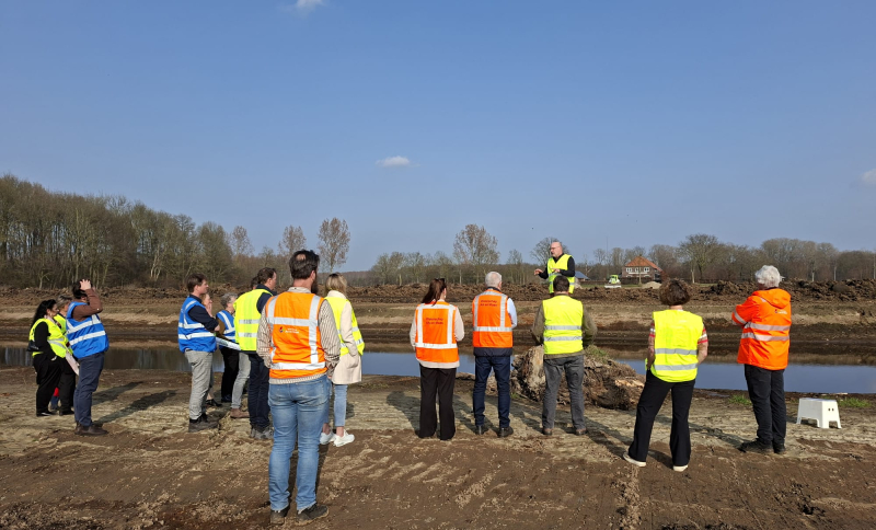 Groep deelnemers met veiligheidshesjes tijdens een veldbezoek aan een gebiedsontwikkelingsproject in Noordoost‑Brabant.