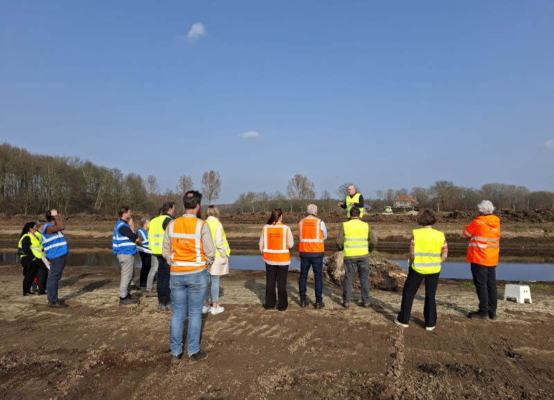 Groep deelnemers met veiligheidshesjes tijdens een veldbezoek aan een gebiedsontwikkelingsproject in Noordoost‑Brabant.