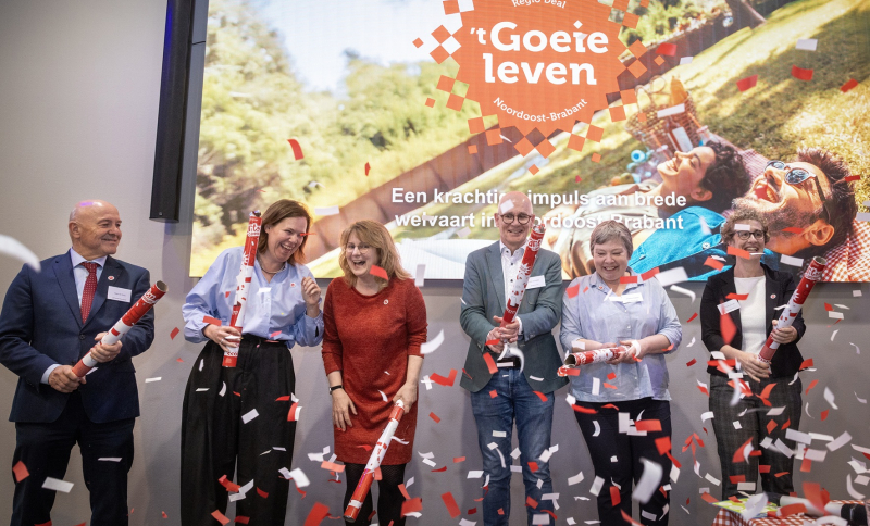 Feestelijk moment tijdens Regio Deal startbijeenkomst bestuurders met confetti op het podium. Op de achtergrond een foto met het Regio Deal logo.
