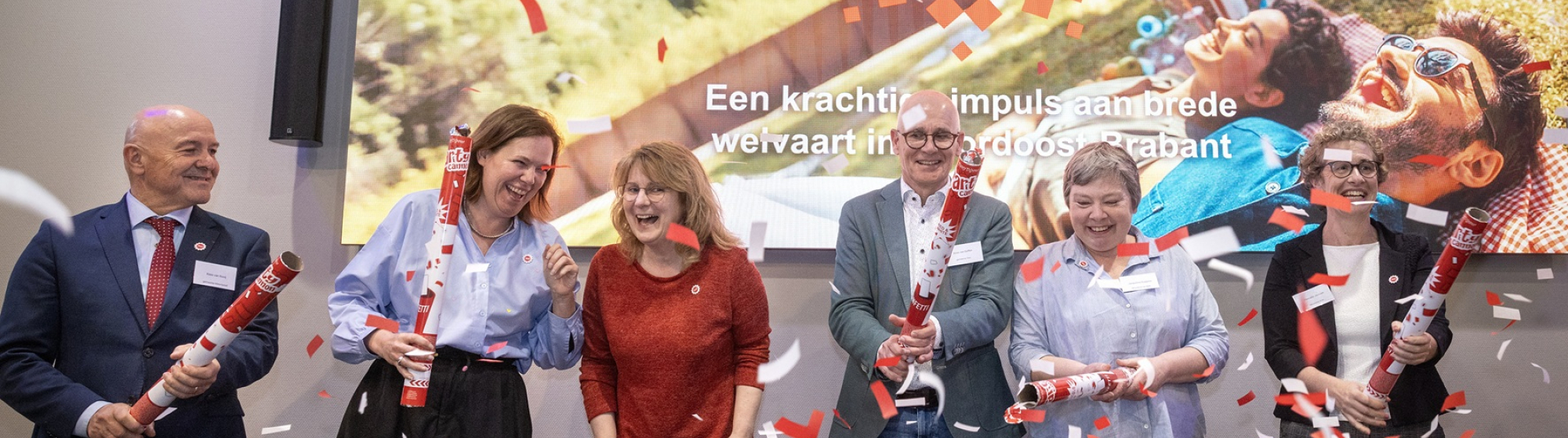Feestelijk moment tijdens Regio Deal startbijeenkomst bestuurders met confetti op het podium. Op de achtergrond een foto met het Regio Deal logo.
