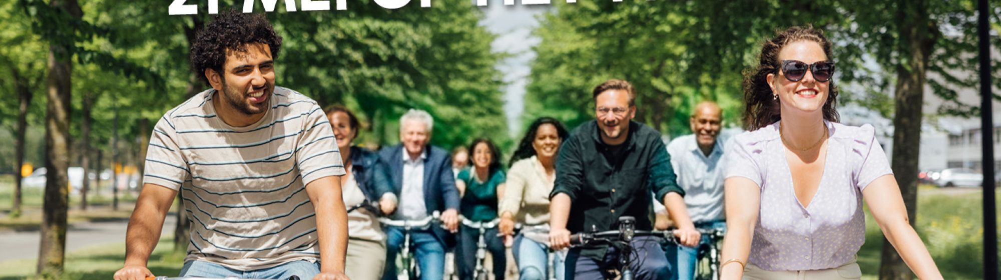 Groep mensen fietst samen door groene laan tijdens Fiets naar je Werk Dag op 21 mei.