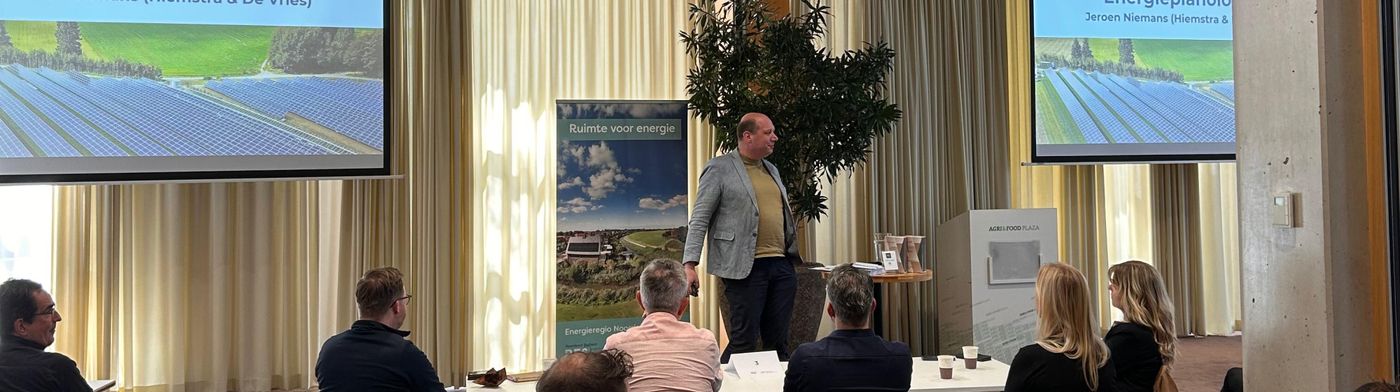 Presentatie over zonne-energie en energietransitie met spreker en deelnemers tijdens workshop met slides van zonnepaneleninstallaties.