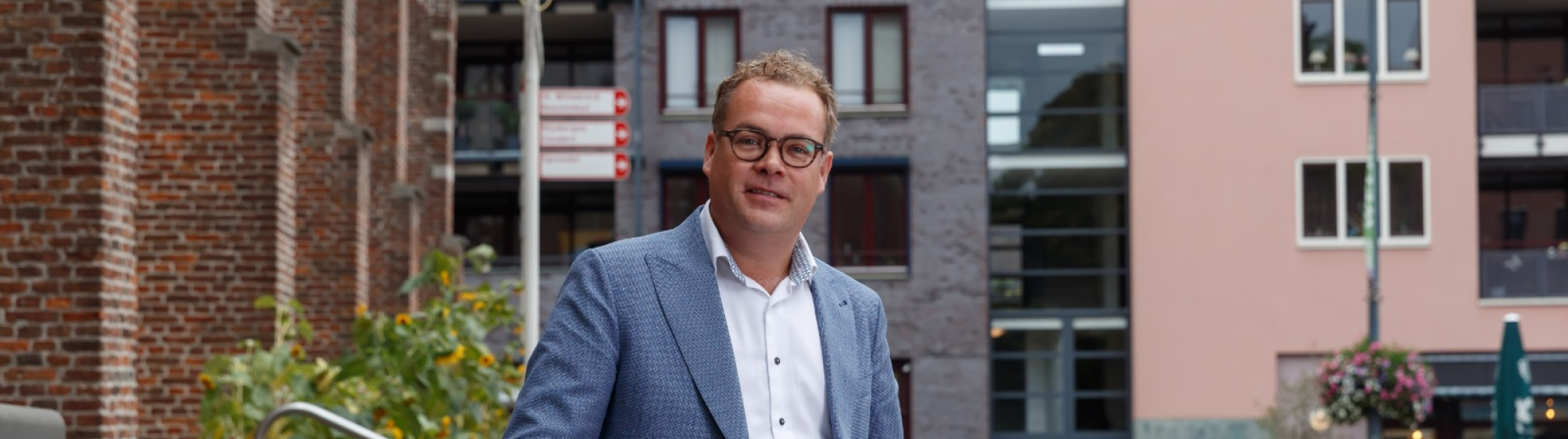 Erik Kiers buiten in stedelijke omgeving met moderne gebouwen en groene beplanting op de achtergrond.