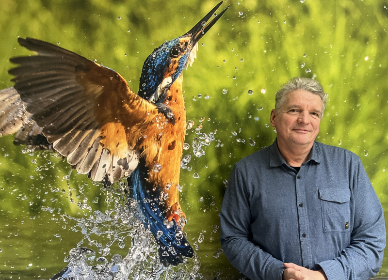 Foto van Ernest de Groot vóór een grote foto van een landschap en een vogel