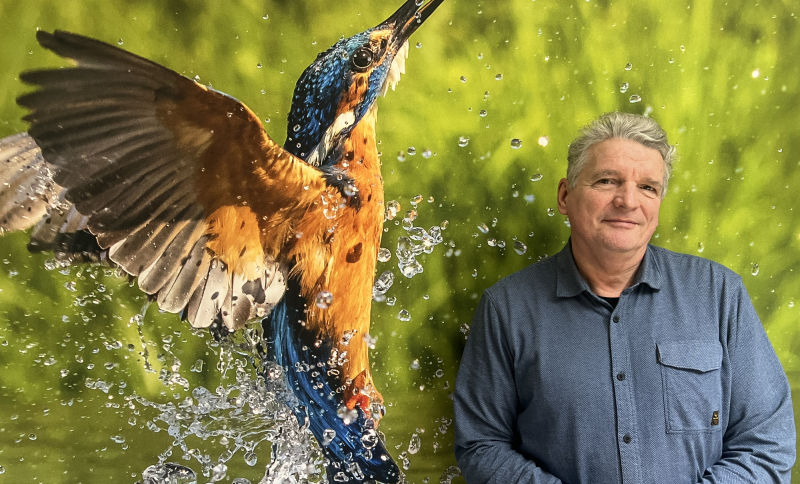 Foto van Ernest de Groot vóór een grote foto van een landschap en een vogel